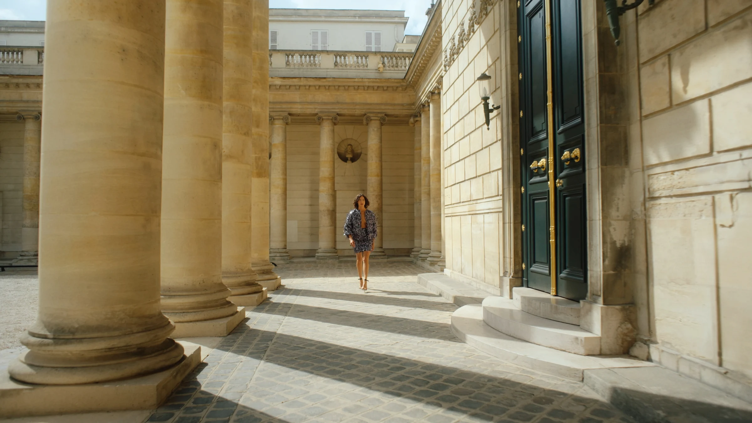 Model walking through a sunlit colonnade