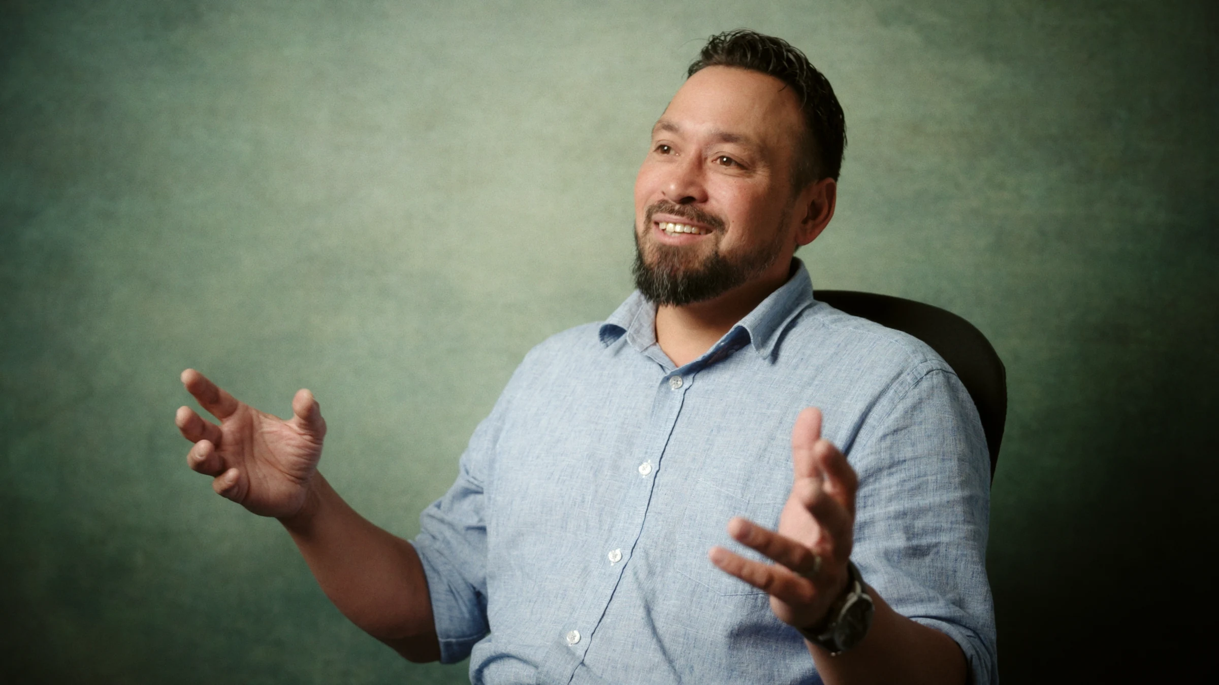 An interviewee gesturing against a soft green background